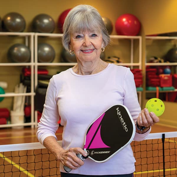 An older woman holding a tennis racket and ball.