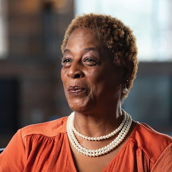 An african-american woman wearing an orange top and pearls.